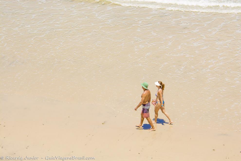 Imagem casal de turistas andando pela beira do mar.